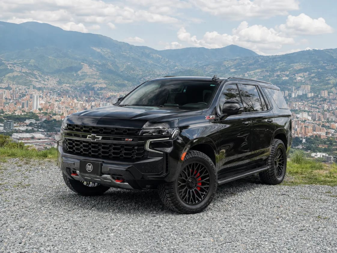 Chevrolet Tahoe negra con rines oscuros, de tres cuartos frontal, sobre un mirador con Medellín y la cordillera al fondo.