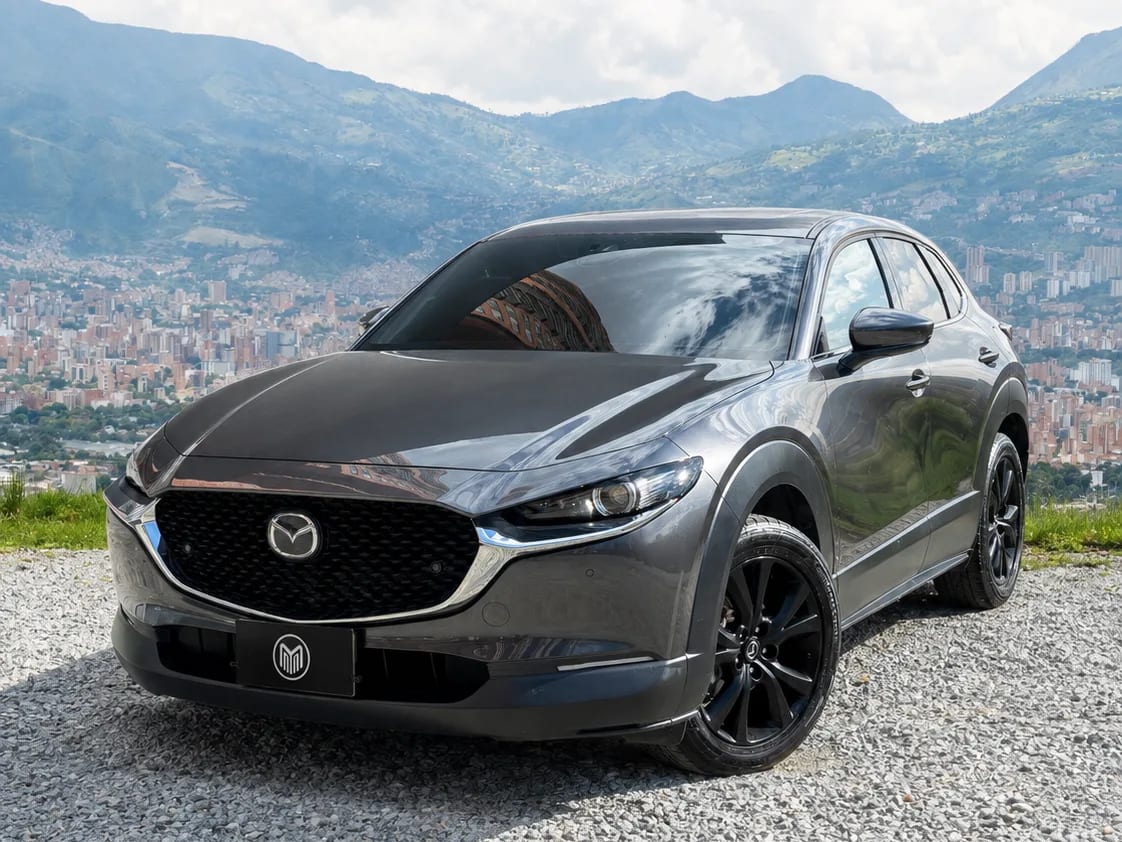 Mazda CX-30 gris grafito con rines negros, de tres cuartos frontal, sobre un mirador con Medellín al fondo.