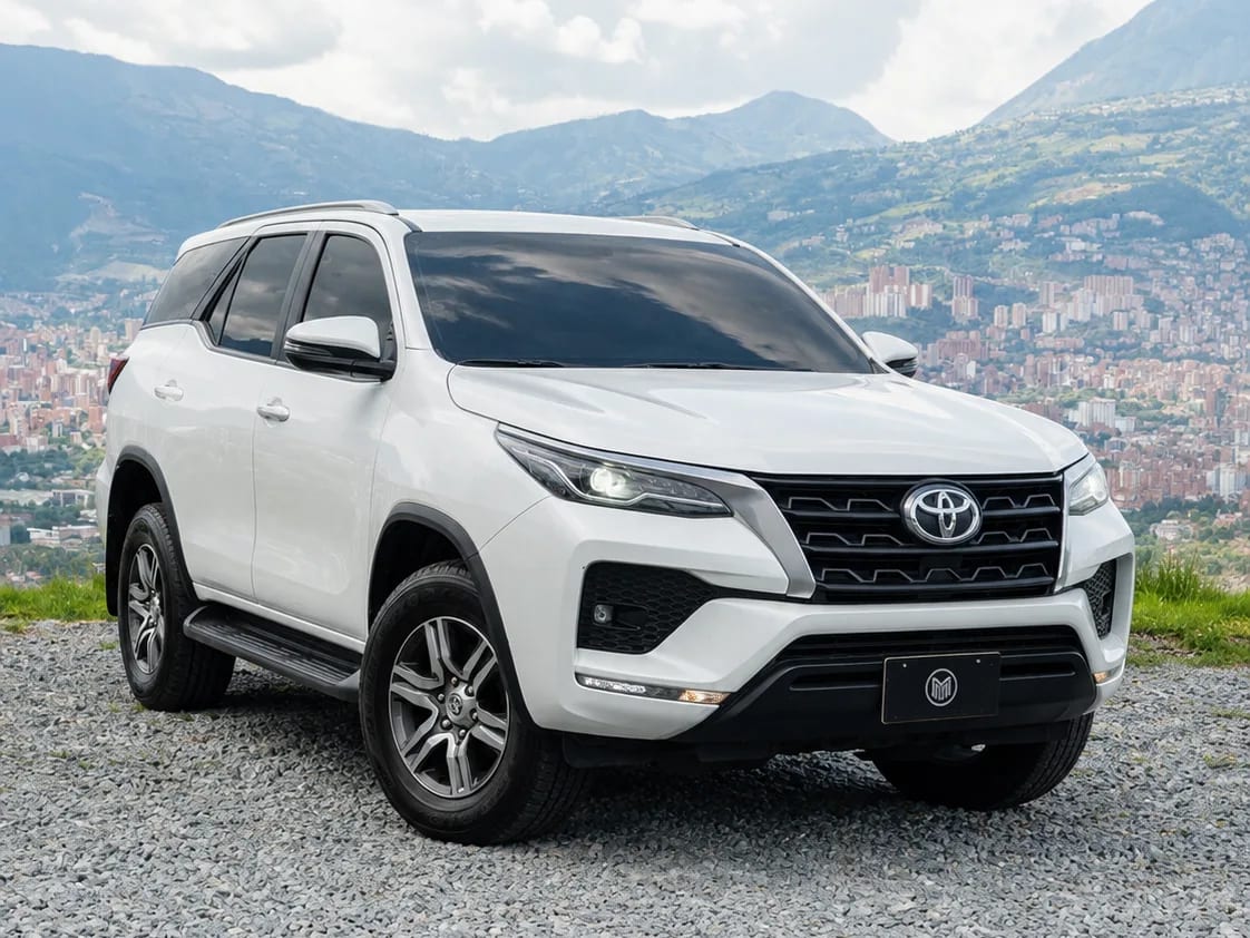 Toyota Fortuner blanca con barras de techo, de tres cuartos frontal, sobre un mirador con Medellín al fondo.